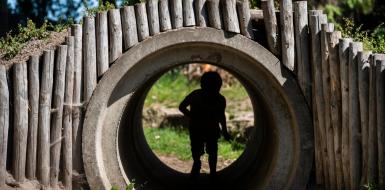 Kind speelt in tunnel of pijp in een speeltuin. Je ziet het kind in de schaduw ervan.